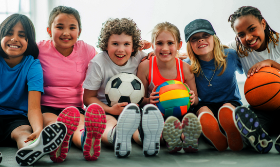 Kinder sitzen auf der Sporthalle auf dem Boden mit Bällen